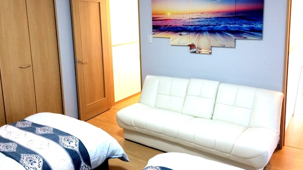 Ett sovrum med en vit soffa, en säng med mönstrat sänglinne och en stor väggmålning som föreställer en solnedgång över havet.