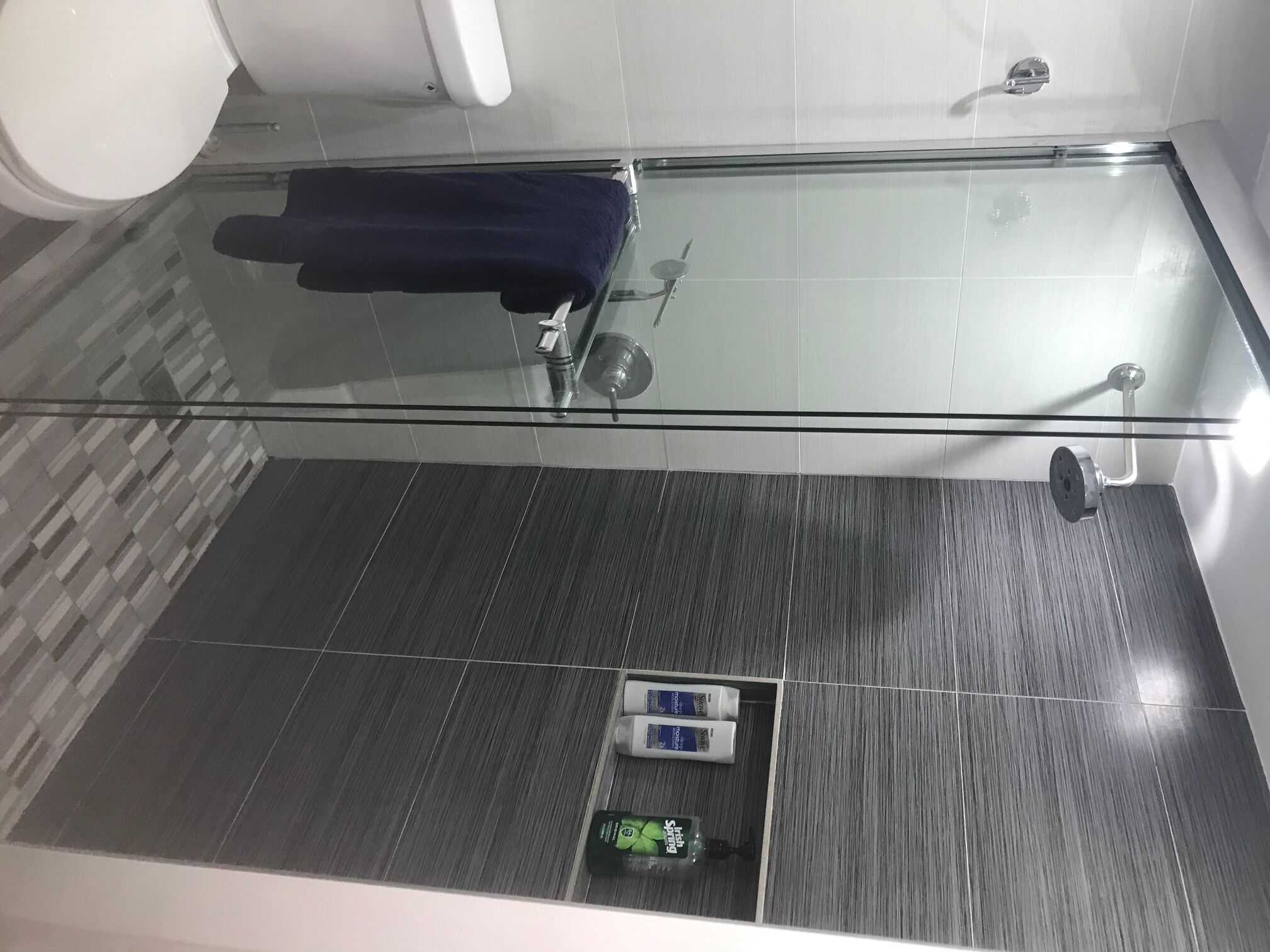A modern bathroom with a glass shower enclosure, a dark wood floor, and a towel rack.