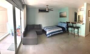 A bedroom with a bed, a sofa, a desk with chairs, and a ceiling fan.