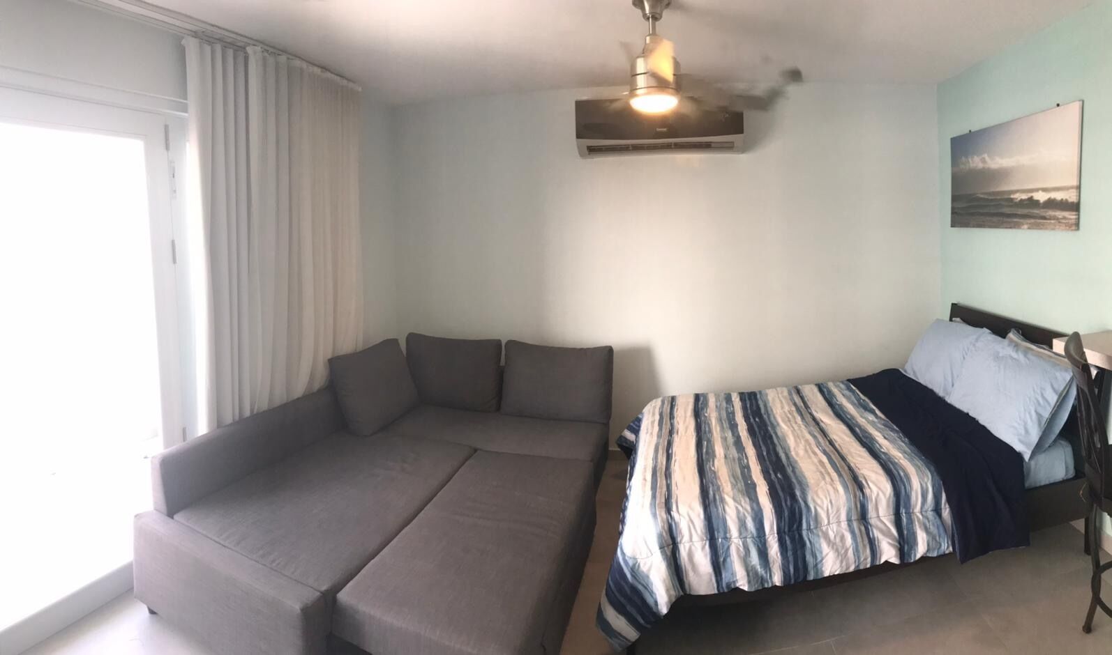 Un dormitorio con cama, sofá, ventilador de techo y ventana con cortinas.