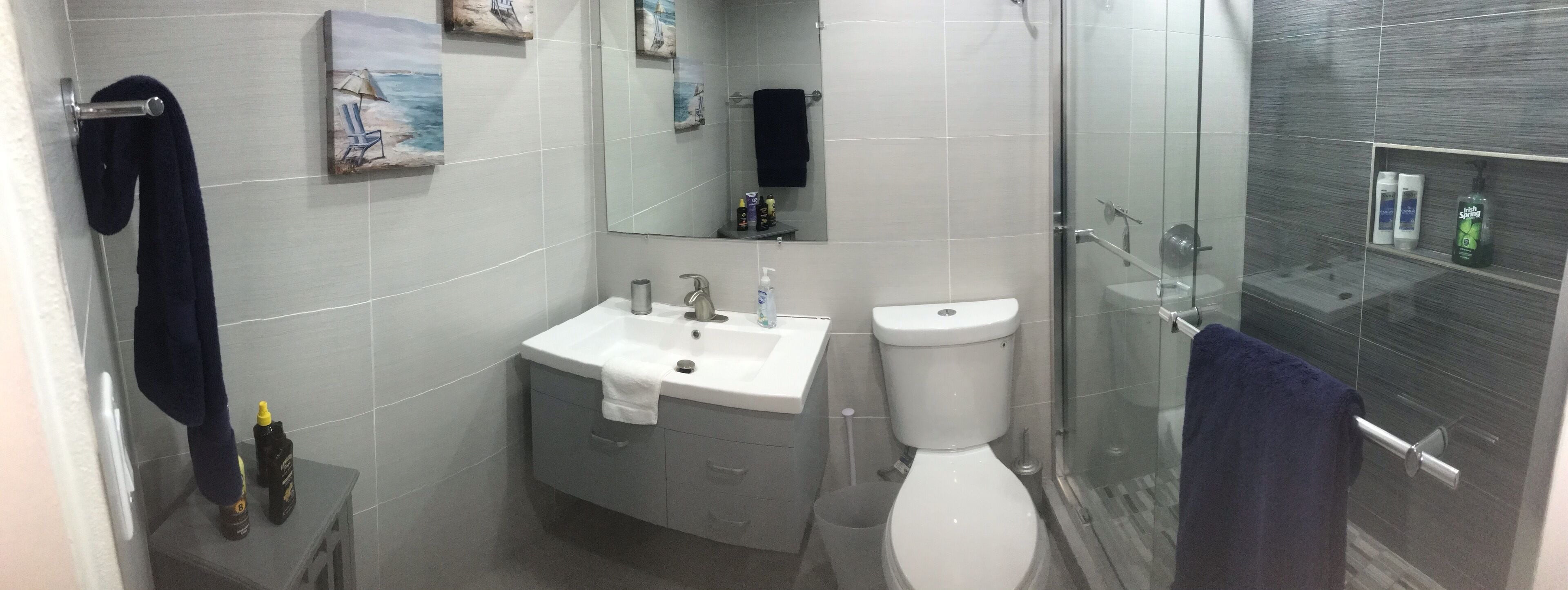 Une salle de bain avec un lavabo blanc, des toilettes et une douche en verre. Des serviettes sont accrochées au mur et une étagère contient des articles de toilette.