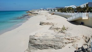 Een strand met een witte omheining, palmbomen en gebouwen langs de kust.