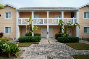 A two-story building with a central entrance, a balcony on the second floor, and a small garden area with plants in front. - "Gorgeous and Open" 2 Bedroom / 2 Bath Villa (Bimini)
