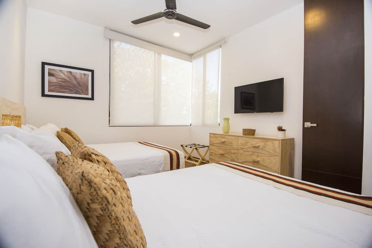 A bedroom with two beds, a ceiling fan, a TV, a window, and a wooden dresser.