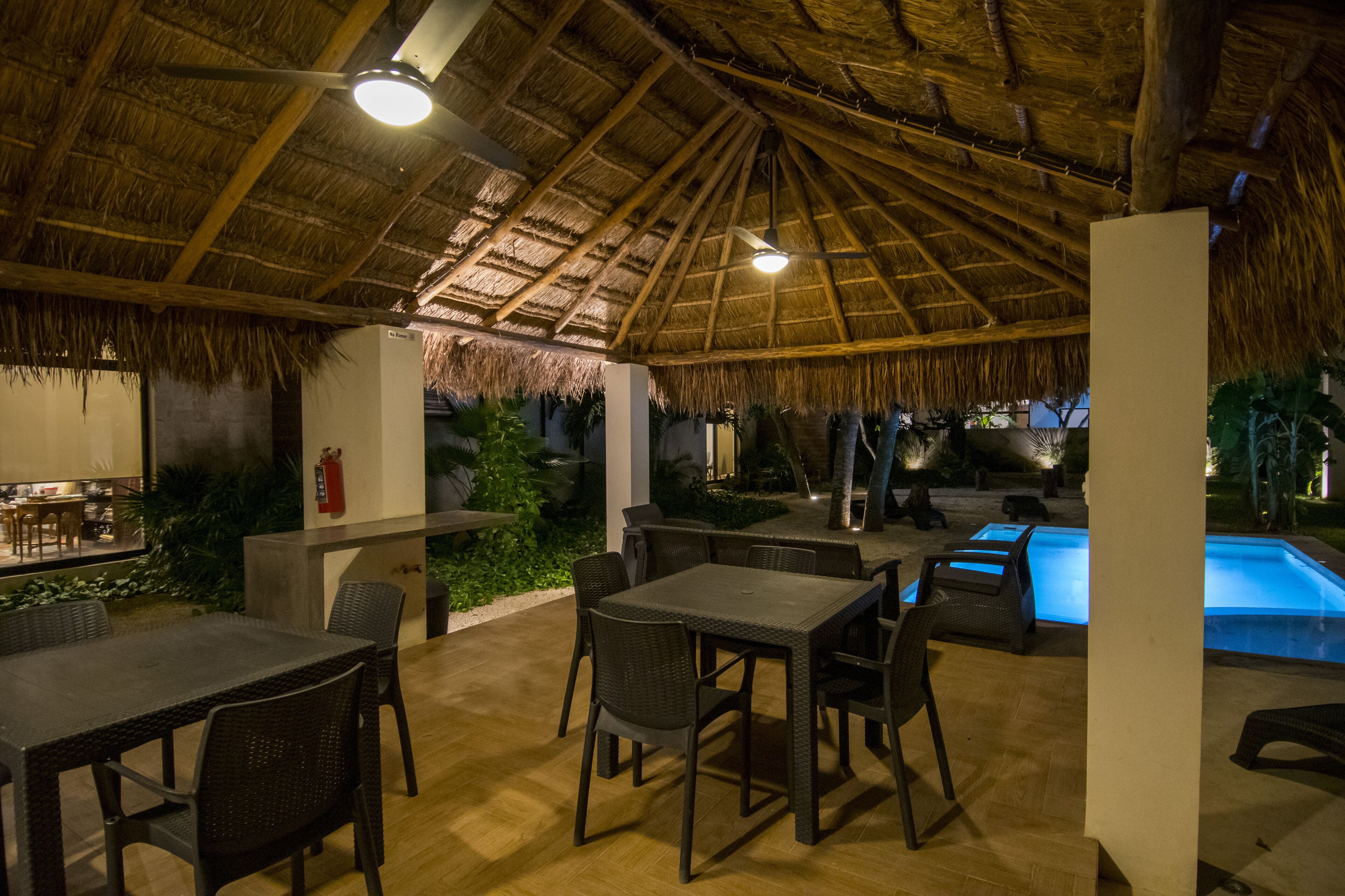An outdoor dining area with thatched roof, tables, and chairs, overlooking a pool.