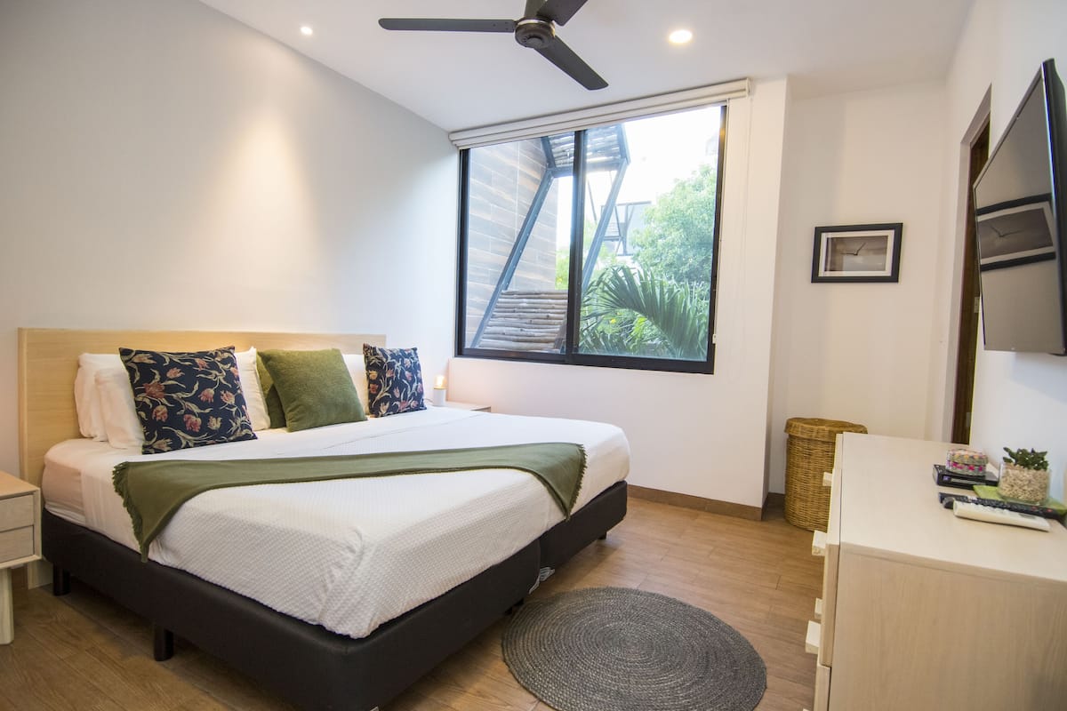 A bedroom with a bed, a desk, a chair, a window, and a ceiling fan.