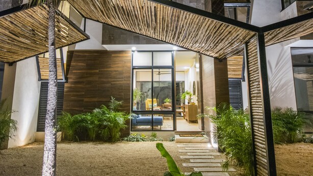 Ein modernes Haus mit überdachter Terrasse, einer Treppe und einem gut beleuchteten Eingang.