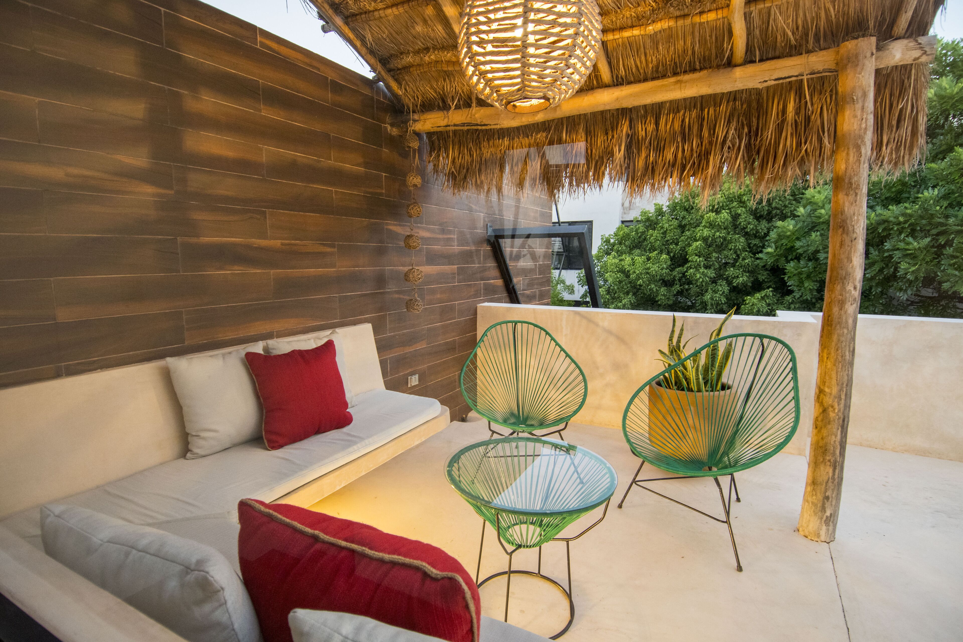 An outdoor seating area with a sofa, two chairs, and a hanging light fixture.