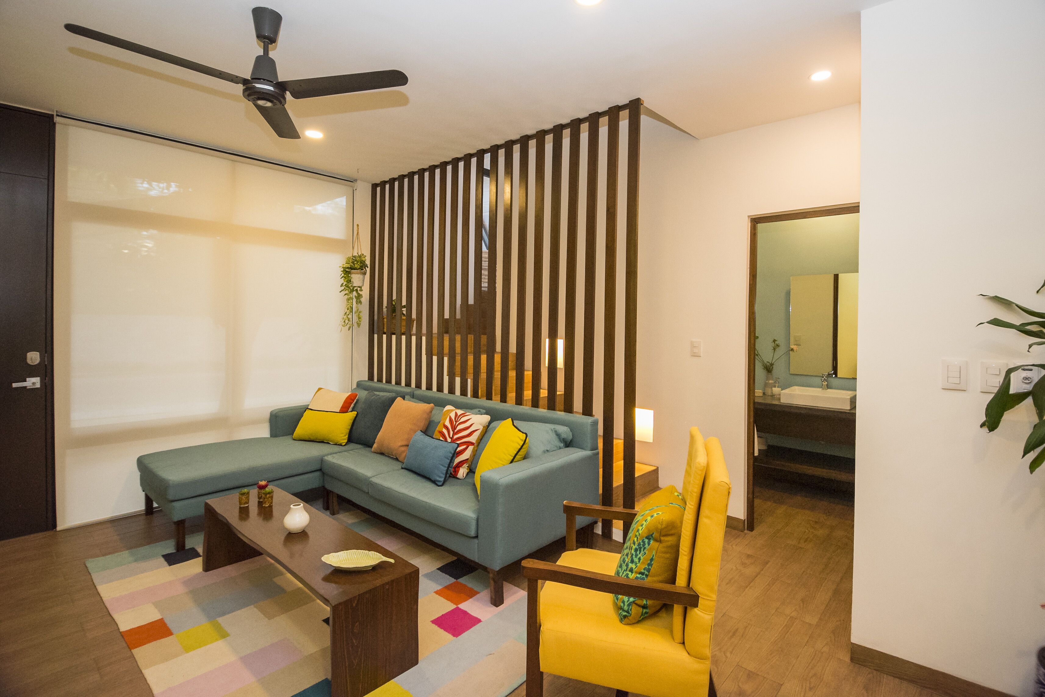 Una sala de estar moderna con un sofá modular, un sillón amarillo, una mesa de centro y un ventilador de techo.