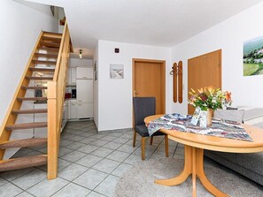 Een woonkamer met een houten trap, een eethoek met een tafel en stoelen, en een keuken op de achtergrond.
