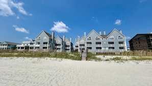 A beachfront hotel with multiple-story buildings, a sandy beach in the foreground, and a clear blue sky. - Cape Coddages I 103 2 Bedroom Condo by RedAwning (Surfside Beach)