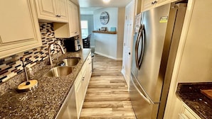A kitchen with white cabinets, granite countertops, stainless steel appliances, and a herringbone-patterned backsplash. - Cape Coddages I 103 2 Bedroom Condo by RedAwning (Surfside Beach)