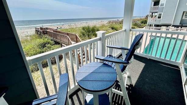 A balcony with a view of the beach, a pool, and a building with balconies. - Cape Coddages I 103 2 Bedroom Condo by RedAwning (Surfside Beach)