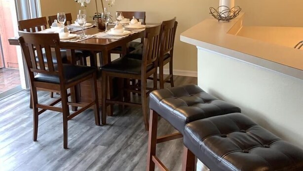 A dining area with a wooden table set for six, a chandelier, and a decorative wall piece.