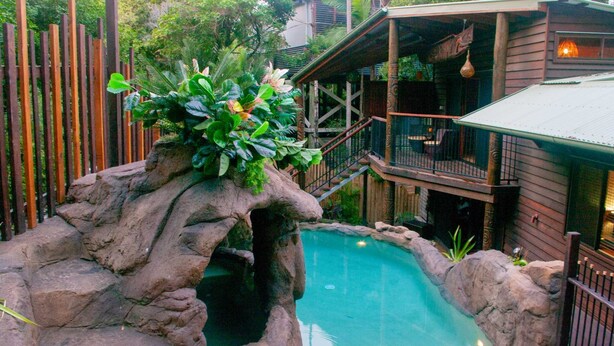 Una piscina con una formación rocosa natural y una terraza de madera con barandilla.
