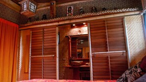 Habitación tradicional con pared de listones de madera, cama con colcha roja y una pequeña estantería con objetos decorativos.