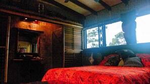 Ein gemütliches Zimmer mit einem Bett, einem Fenster mit dekorativem Gitterwerk und einem kleinen Tisch mit Büchern und einer Lampe.