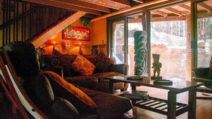 Una habitación acogedora con techo de madera, un sofá con cojines estampados, una mesa con un jarrón y un ventanal con vistas a un jardín.