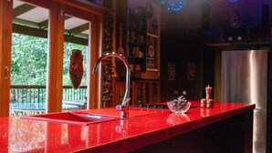 Una cocina con encimera roja, un lavamanos de acero inoxidable y un cuenco decorativo con fruta.