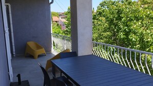 Een terras buiten met een tafel, stoelen en een gele kruk, plus een metalen reling.