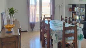 Een eethoek met een tafel, stoelen, een boekenkast en een uitzicht door een raam.