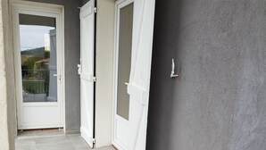 Een gang met grijze betegelde vloer, witte deuren en uitzicht op een balkon.