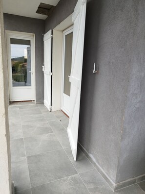 Un couloir au sol carrelé de gris, avec des portes blanches et une vue sur un balcon.