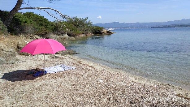 Een strand met helder water, een roze parasol en een rotsachtige kustlijn.