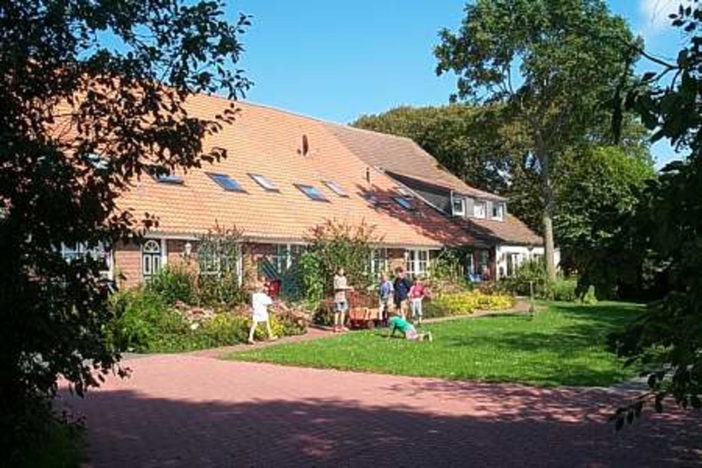 Een gebouw met een pannendak, een verhard pad en een gazon met mensen.