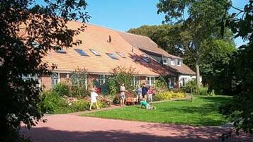 Een gebouw met een pannendak, een verhard pad en een gazon met mensen.