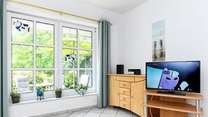 A room with a TV on a wooden stand, a window with curtains, and a tiled floor.