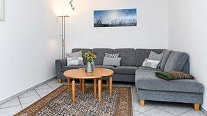 A modern living room with a grey sofa, a round wooden coffee table, a floor lamp, and a framed picture on the wall.