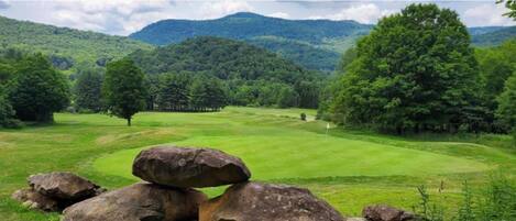 Un paisaje verde y exuberante con colinas ondulantes, cielo despejado y un campo de golf.