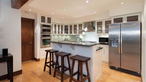 Eine moderne Küche mit weißen Schränken, einem Edelstahlkühlschrank und Holz-Barkeckstühlen.
