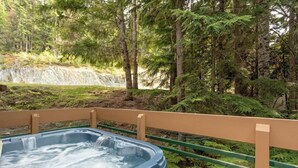Ein Whirlpool, umgeben von einer Holzterrasse und bewaldeter Landschaft mit einem Wasserfall im Hintergrund.