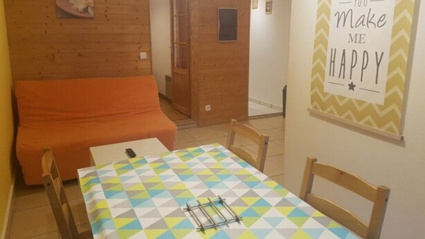 Una habitación con pared de madera, una cama, una mesa con mantel estampado y un cartel motivacional.