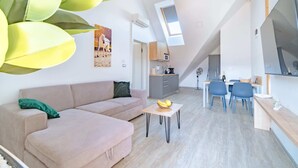 Una sala de estar moderna con un sofá, una zona de comedor con sillas, una pequeña mesa con fruta y una cocina al fondo.
