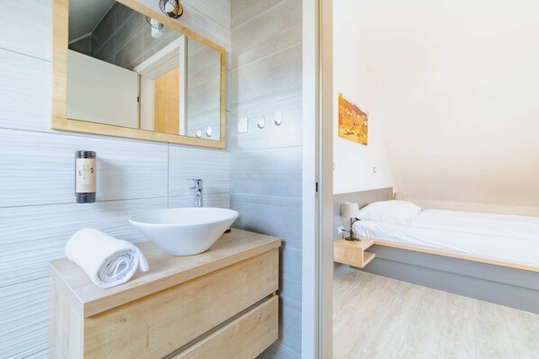 Un baño moderno con un lavamanos blanco, tocador de madera y un espejo grande.