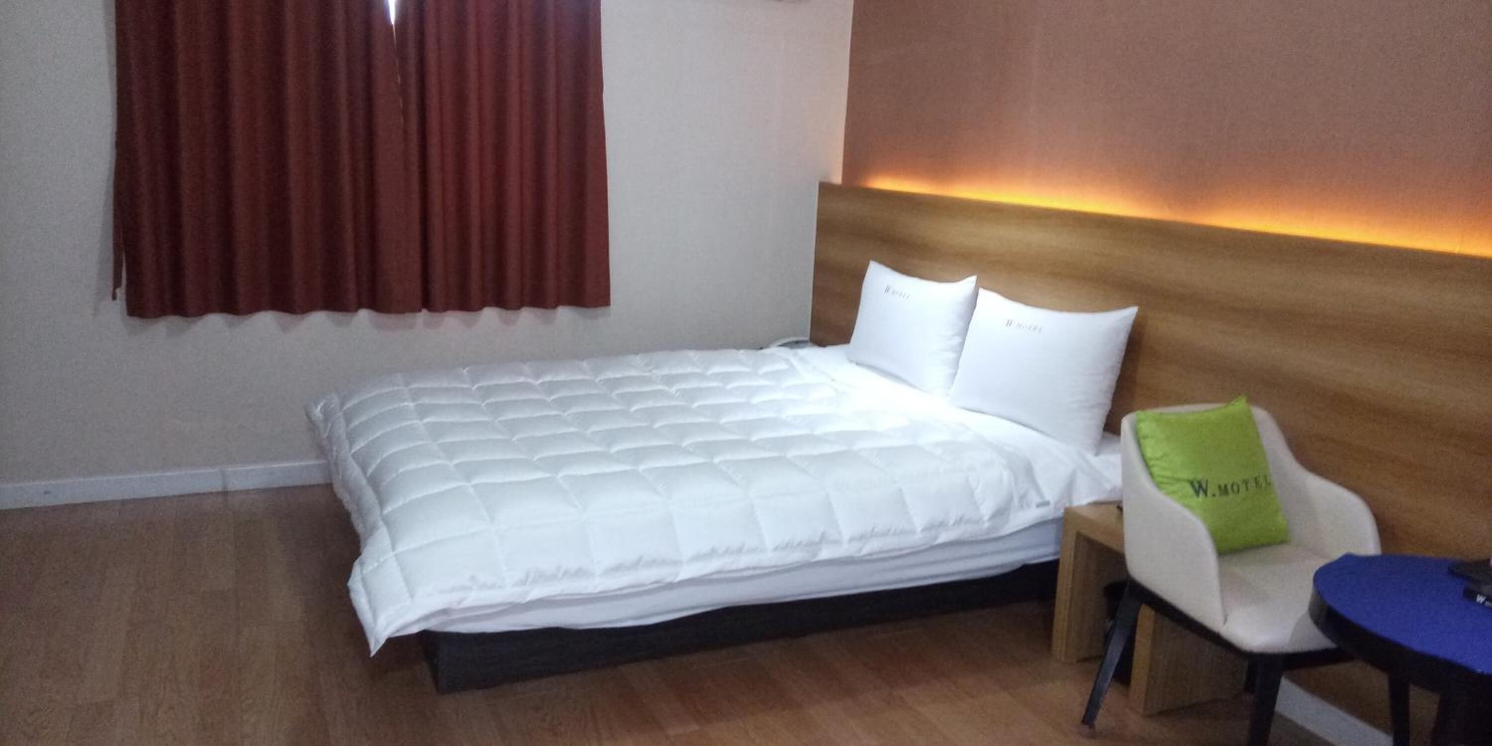 Una habitación de hotel con cama, una silla, una mesita y una ventana con cortinas.