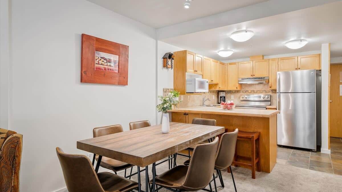 A modern kitchen with wooden cabinets, stainless steel appliances, and a dining area with a wooden table and chairs.