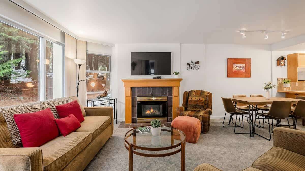 A modern living room with a fireplace, a TV mounted above it, and a dining area with a table and chairs.