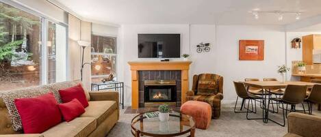 A modern living room with a fireplace, a TV mounted above it, and a dining area with a table and chairs.