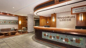 A reception area with a wooden reception desk, a stone pillar, and a sign for Woodrun Lodge. - Forest condo w/ AC, pool & gym (Whistler)