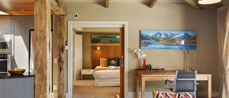 A hotel room with a bed, a desk, a chair, a painting, and a view of a mountain landscape.