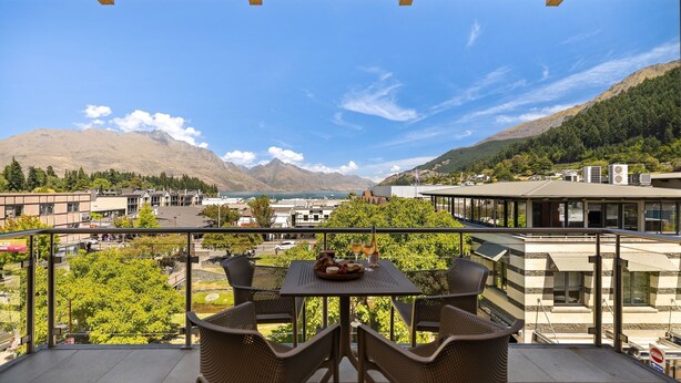 Un balcon avec une table et des chaises, donnant sur un paysage montagneux avec des bâtiments visibles au loin.