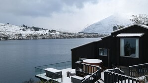A cabin with a balcony overlooking a lake, surrounded by snow-covered hills. - Queenstown Lakefront Dream | 4 Bed (Queenstown)