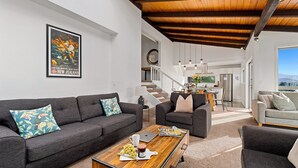 A modern living room with a dark grey sofa set, a coffee table with a magazine and a laptop, and a framed poster on the wall. - Queenstown Lakefront Dream | 4 Bed (Queenstown)