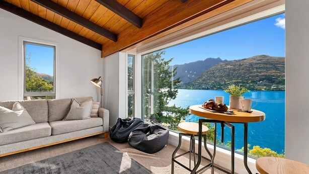 A modern living room with a sofa, a coffee table, and a view of a lake and mountains. - Queenstown Lakefront Dream | 4 Bed (Queenstown)