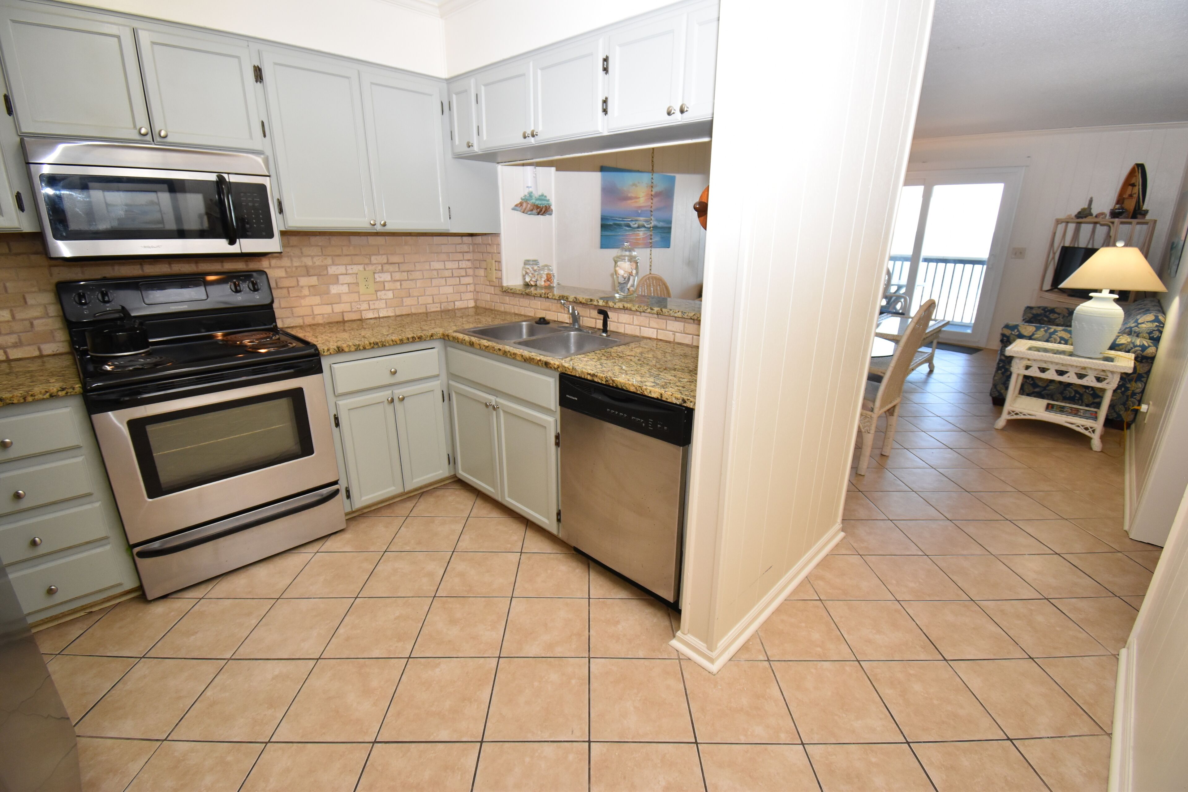 A kitchen with white cabinets, a microwave, stove, dishwasher, and a tiled floor.