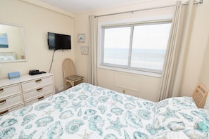 A bedroom with a bed, a dresser, a chair, a television, and a window with blinds.